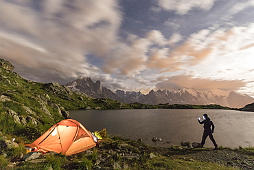 Hiker and tent on the shore of Lacs De Cheserys at night with Mont Blanc massif in background, Chamonix, Haute Savoie, France, French Alps, Europe