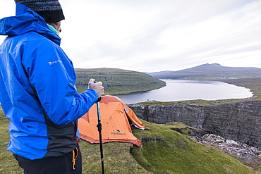 Hiker on cliffs looks towards lake Sorvagsvatn, Vagar Island, Faroe Islands, Denmark, Europe