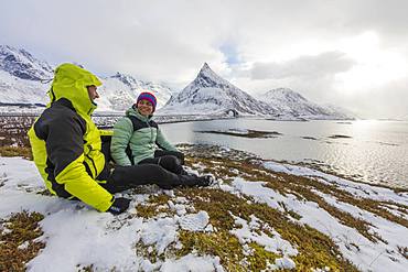 Hikers on meadows covered with snow with Volanstinden in the background, Fredvang, Lofoten Islands, Nordland, Norway, Europe