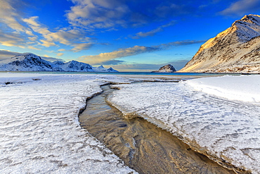 The golden sunrise reflected in a clear stream of the sea where the snow has melted, Haukland, Lofoten Islands, Arctic, Norway, Scandinavia, Europe