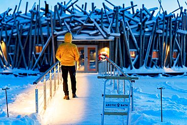 Person standing on the frozen walkway at dusk connecting the floating Arctic Bath Hotel to the shore, Harads, Lapland, Sweden