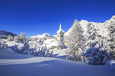 The winter sun illuminates the snowy landscape and the typical church, Maloja, Engadine, Graubunden (Grisons) Canton, Switzerland, Europe