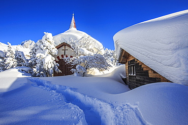 The small church and the house submerged by snow after a heavy snowfall in Maloja, Engadine, Graubunden (Grisons) Canton, Switzerland, Europe