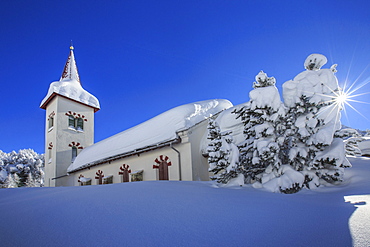 Rays of winter sun illuminate the snowy landscape and the typical church, Maloja, Engadine, Graubunden (Grisons) Canton, Switzerland, Europe