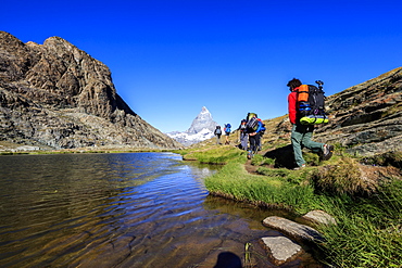 Hikers proceed on the shore of Lake Riffelsee with the Matterhorn in the background, Zermatt, Canton of Valais, Switzerland, Europe