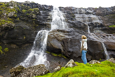 Woman looking at a waterfall in Estuyroy, Faroe islands, Denmark