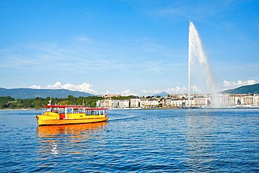 Yellow water taxi ???Mouettes genevoises??? on the calm waters of Lake Geneva with tourist attraction Jet d'eau in the background