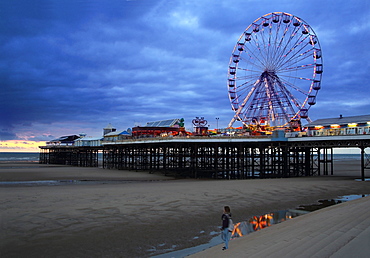 Big wheel and amusements on Central Pier at sunset with young women looking on, Blackpool, Lancashire, England, United Kingdom, Europe