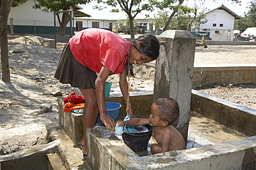 East timor. Camp for internally displaced people (idps) at the don bosco center in dili. Girl collecting water and washing baby at faucet