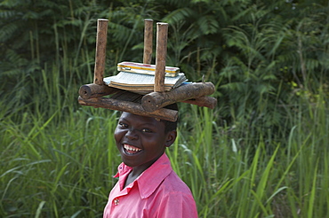 South sudan student of lutaya primary school walking to school with her books and stool to sit on as there is usually no furniture in the classrooms. yei