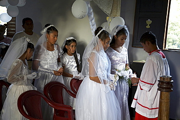 Guatemala catholic first communion and mass at remate, el peten. altar boy lights candles of young girls after the ceremony