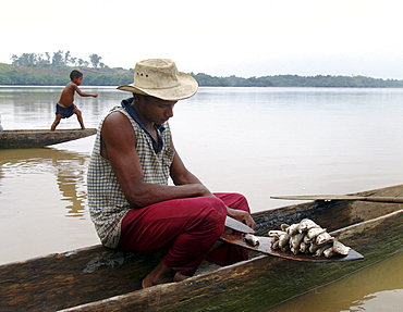 Colombia fisherman cleaning fish while he sits in his dugout canoe. A boy fishing with a line in the background. Rio magdalena, barrancabermeja