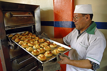 Colombia baker taking rolls out of the oven of his bakery in ciudad bolivar, bogota