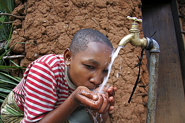 Tanzanian girl drinking water from the family tap. Mvango village, same, in the north-east near kilimanjaro