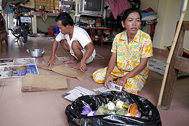 CAMBODIA HIV+ couple making handicrafts. Toul Sambo village is a resettlement area outside of Phnom Penh. Set in rural tranquility surrounded by paddy fields, it is a peaceful place for its residents. A Caritas Cambodia project, it has two focus groups who live there. One group is largely HIV+ and used to reside in a Phnom Penh slum called Borey Kila, until they were evicted by the government who wanted to develop the land for offices and shopping malls. The other group consists of those made homeless when a river's bank subsided in their village, destroying their homes. At the home of Kea Nimal and Kem Sokhorn, both HIV+. They are very industrious working at home making paper bags and ornaments, some with recyclable materials. They can earn $12-$15 per 5-day working week, and live quite comfortably in their attractive home with TV, motor-cycle and other conveniences. They say they are much better off than in the crowded and unhealth slum of Borey Kila in Phnom Penh where they used to live. They get regular orders for the handicrafts they make. They stay healthy by taking ARVs, which are supplied free of charge by the Hope Organization. PHOTO by Sean Sprague