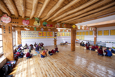 A light-filled elementary classroom. A white ceiling reflects light from the windows above. Traditional building methods and materials, such as the poplar and willow ceilings are combined with modern solar and passive solar technology. Druk Padma Karpo Institute. Shey, Ladakh, India