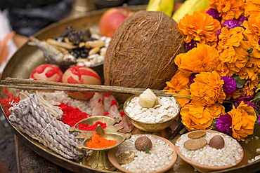 A brass plate full of offerings to God. Coconut, dried fish, black soya beans, duck eggs, oiled wicks, colour powder, bitten rice, betel nut, hand made rice paper incense, unhusked rice and flowers. Brahmayani Temple, Bhaktapur, Nepal