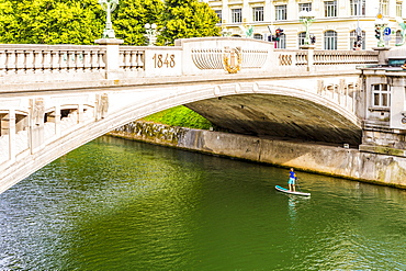 A boy paddle-boarding under Dragon Bridge, Ljubljana, Slovenia, Europe