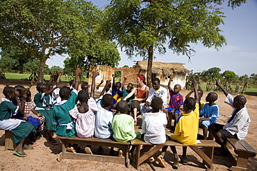 Volunteer Primary Cluster Teacher trainer, Fiona Stevenson leading story time and singing in the yard of primary school in Fori, next to trainee Alpha Ajallow,  The Gambia, West Africa, Africa