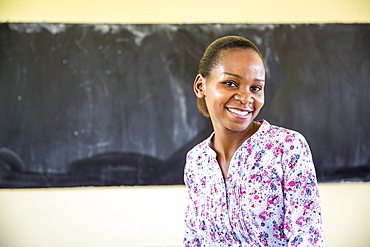 Local teacher Rebecca Ngovano sitting in front of a blackboard in one of the classrooms of Angaza school, Lindi, Tanzania, East Africa, Africa