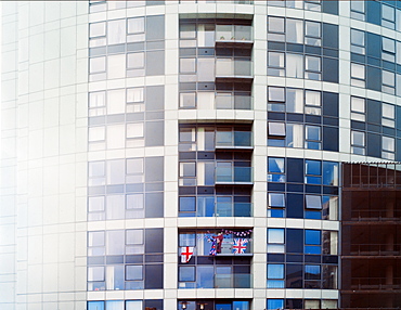 A patriotic woman waves flags from her balcony in a block of flats, United Kingdom, Europe