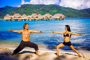 Couple doing yoga in front of overwater bungalows, Le Taha'a Resort, Tahiti, French Polynesia, South Pacific, Pacific