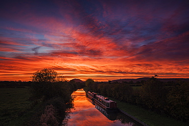 Barges lay still on the Shropshire Union canal as the dawn light sweeps across the sky above Beeston Castle, Cheshire, England, United Kingdom, Europe