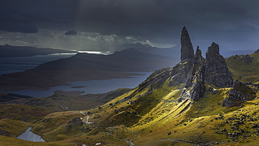 A burst of light briefly illuminates the pinnacles surrounding the Old Man of Storr against an approaching storm, Isle of Skye, Inner Hebrides, Scotland, United Kingdom, Europe