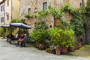 People sitting outside at a restaurant within a small courtyard surrounded by flowers in Pienza, Tuscany, Italy, Europe