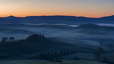 Pre-dawn mist lies in the fields and hills of the Val d'Orcia beyond a farmhouse perched on top of a small outcrop, UNESCO World Heritage Site, Tuscany, Italy, Europe