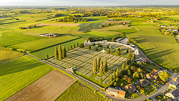 Looking down on the WW1 Tyne Cot cemetery bathed in evening light with Passchendaele village beyond in the Flanders countryside.