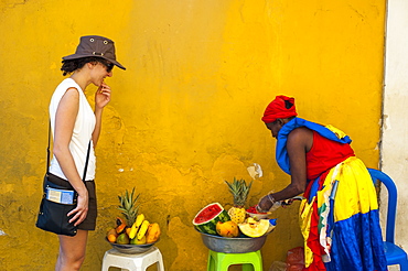 Woman dressed in traditional clothes cutting and selling fruit in the colorful old town of Cartagena, Colombia, South America