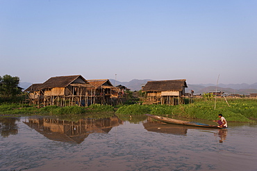 A man paddles his canoe past one of the floating villages on Inle Lake, Myanmar (Burma), Asia