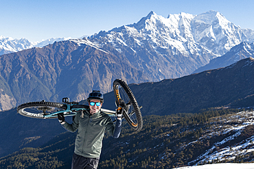 A mountain biker carries his bike up in the Himalayas with views of the Langtang range in the distance, Nepal, Asia