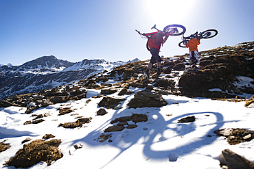 Mountain bikers carry their bikes up a snow covered hillside in the Nepal Himalayas with views of the Langtang mountain range, Nepal, Asia