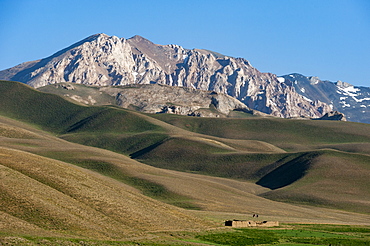 A distant house in the grasslands with views of mountains in the distance, Bamiyan province, Afghanistan, Asia