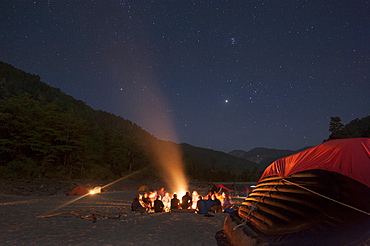 Sitting around a campfire next to the Karnali River during a rafting expedition in Nepal, Asia