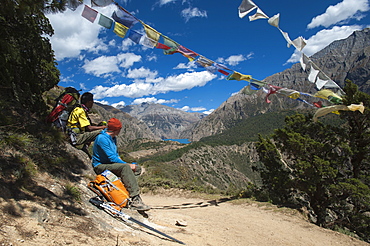 Prayer flags mark a high point in the trail where trekkers are rewarded with their first glimpse of Phoksundo Lake, Dolpa Region, Himalayas, Nepal, Asia