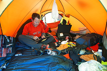 An Everest expeditioner sits among his mountain of equipment while he checks his email with a satelite modem, Khumbu Region, Nepal, Asia