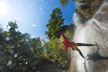 A man pauses to hold his arms in the falling water while canyoning in Nepal, Asia