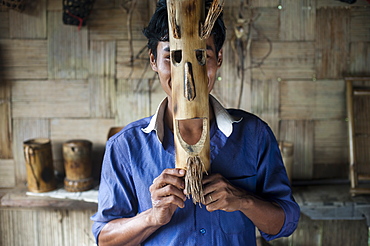 A young man holds a mask made from bamboo to his face, Assam, India, Asia