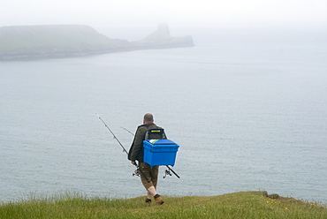 A fisherman walking towards Worms Head from Rhossili Bay on The Gower in South Wales, United Kingdom, Europe