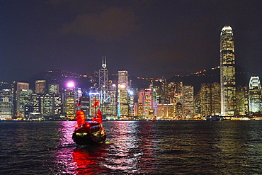 Traditional junk boat on Victoria Harbour with city skyline behind illuminated at night, Hong Kong, China, Asia