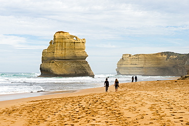 People walk along a beach with one of the Twelve Apostles geological formation in the background, Victoria, Australia, Pacific