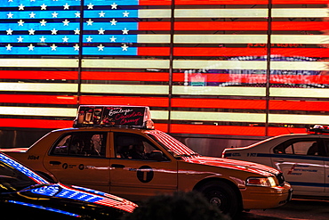 Yellow New York taxi in front of the American flag in Times Square, New York City, United States of America, North America