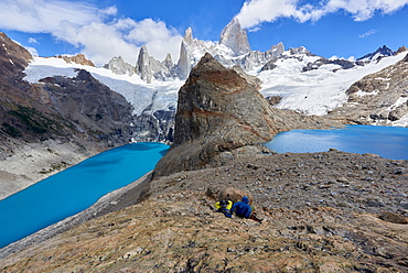 A couple in mountain gear rests on rocks with view to Lago de los Tres and Mount Fitz Roy, Patagonia, Argentina, South America