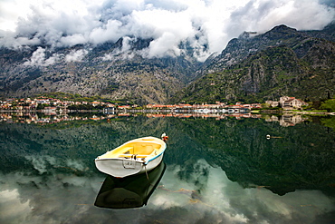 A small fishing boat sits in the reflection of the Old Town (stari grad) of Kotor in Kotor Bay, UNESCO World Heritage Site, Montenegro, Europe