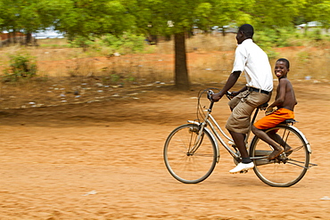 A school boy gets a lift home on the back of a bicycle, Ghana, West Africa, Africa