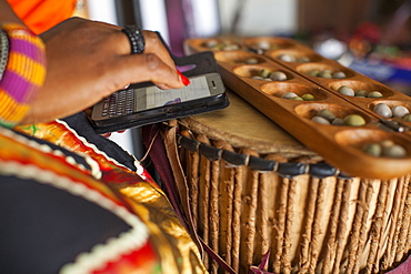 A woman types a message on her mobile phone whilst playing a traditional Nigerian game called Ayo, Nigeria, West Africa, Africa