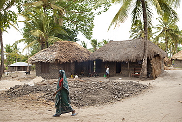 A woman walks past a traditional mud hut home with a solar panel on the top of it, Tanzania, East Africa, Africa